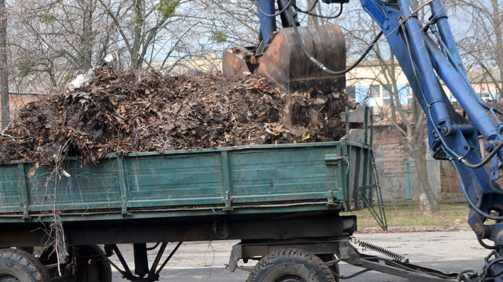 Cleaning dry branches and grass on city streets loading into truck trailer. Cleaning dry leaves tractor bucket. Old tractor bucket picks up old and dry branches and leaves and plunges it into a truck.