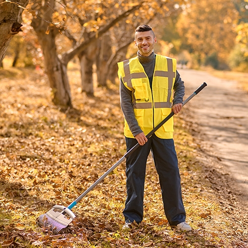 Autumn. A man in a yellow vest raking leaves in the park