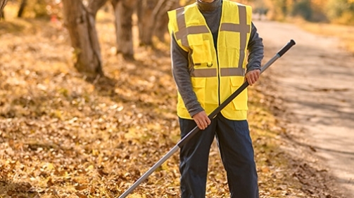 Autumn. A man in a yellow vest raking leaves in the park