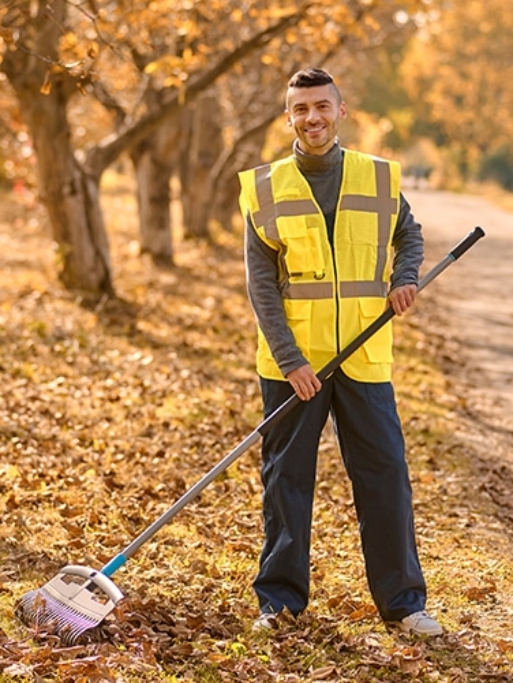 Autumn. A man in a yellow vest raking leaves in the park